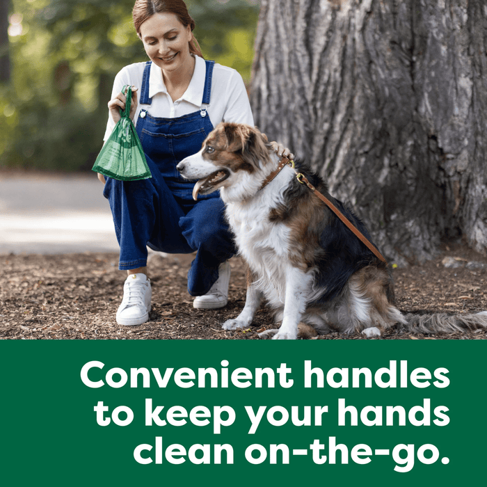 Picture of a woman in blue dungarees and a white t-shirt, knelt down next to a brown and white collie type type dog on a lead. The woman has a green tie handled Earth Rated poop bag in her hand. Text below read 'convenient handles to keep your hand clean on-the-go'.